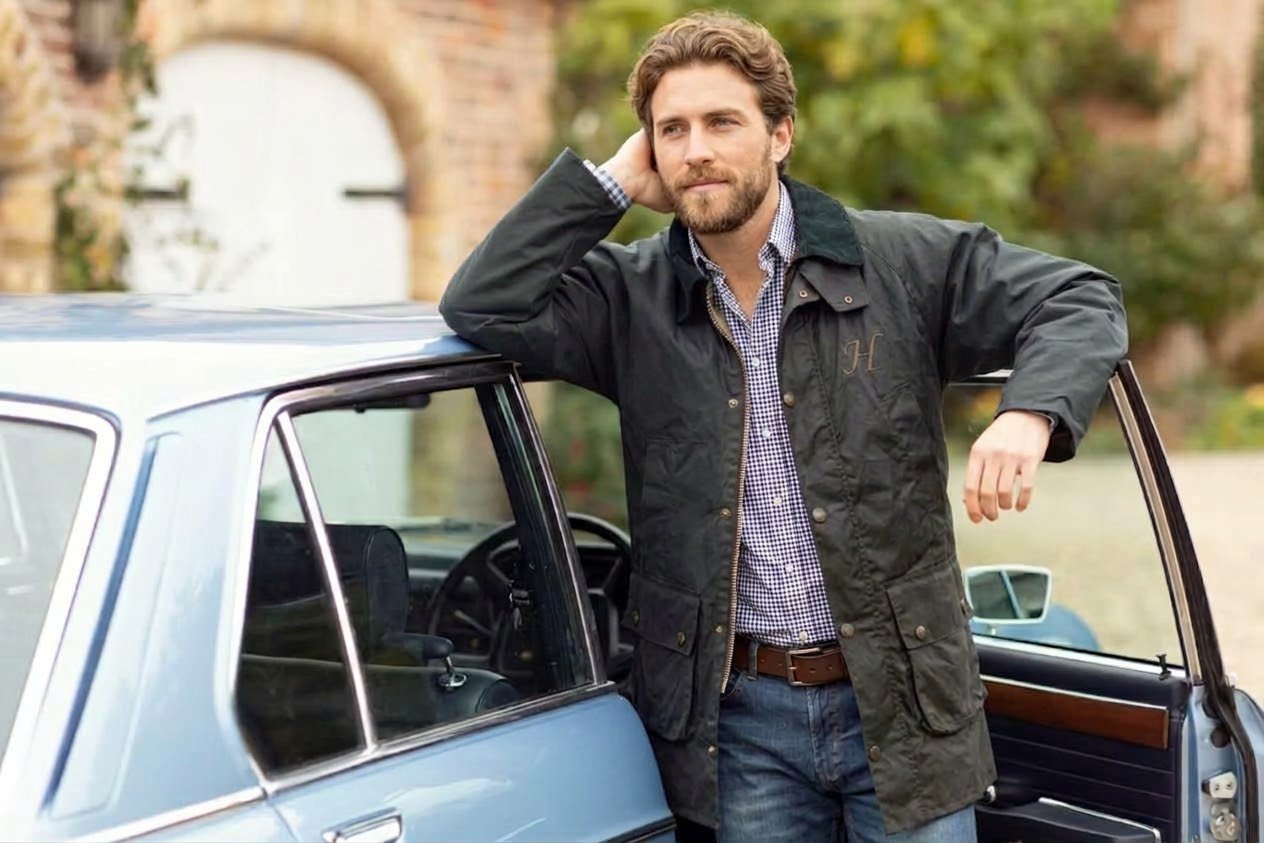 Drover field coat in olive wax with bellows pockets and the Harland H, leaning on a classic car