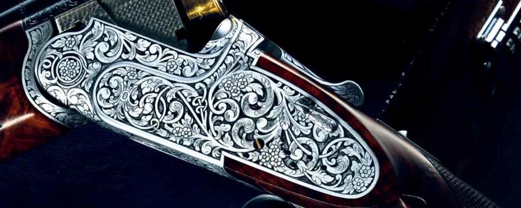 Deep floral scroll hand-engraved across an over-and-under receiver, cartridges in the open breech